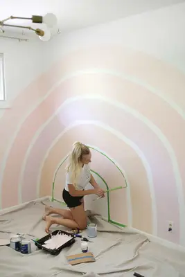 different colored strips of the rainbow on the white wall with someone peeling the green painters tape off the wall