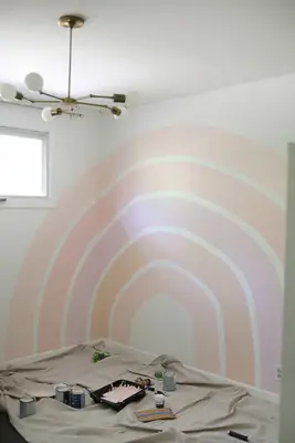 5 painted strips of the rainbow on a white wall with paint cans on floor