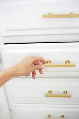 someone opening a white cabinet with gold handles