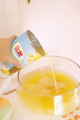 pouring pineapple juice into rainbow sherbet punch