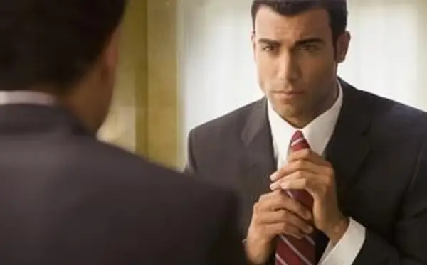 Uomo in giacca e cravatta che aggiusta la cravatta allo specchio