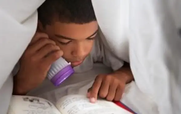 Menino lendo livro sob o cobertor