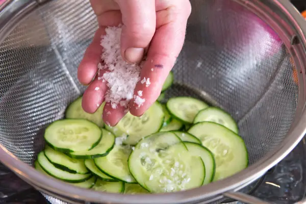 Sprinkling salt over sliced cucumber