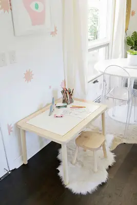 closed wooden sensory table with colored pencils and drawings on it with a wooden stool on a white rug