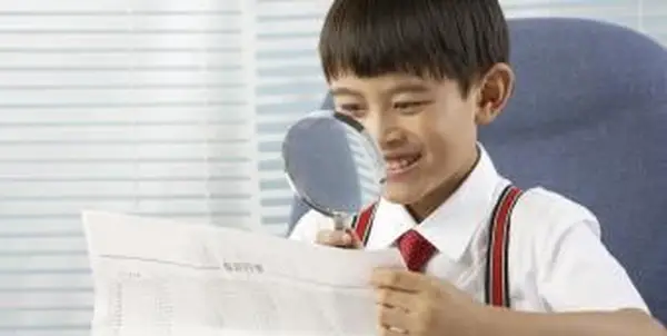 Um menino lendo jornal com uma lupa