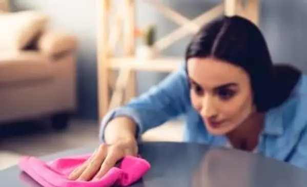 La mujer está utilizando un trapo mientras limpia muebles en casa