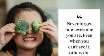 Dívka s rukou držící brokolici před její oči a usmívá se