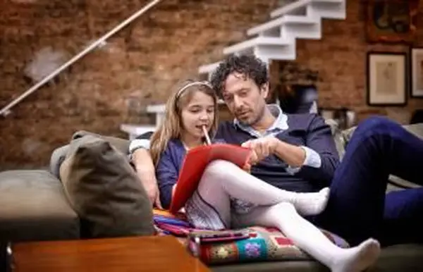 אבא עוזר לבת בשיעורי בית על הספה