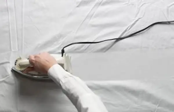 ベッドでアイロンをかける女性
