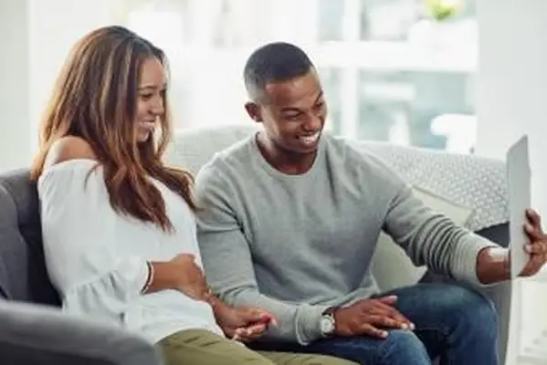 pareja de videollamadas usando una tableta para compartir la noticia de que esperan un bebé en casa