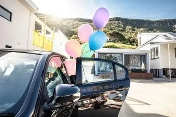 Mujer sosteniendo globos de colores de bebé fuera de un coche