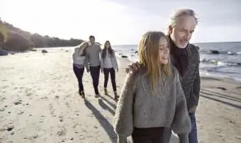 Padrasto e filha passeando na praia com a família ao fundo