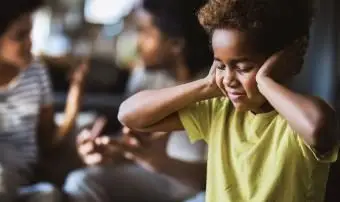 Menina cobrindo as orelhas enquanto se recusa a ouvir os pais discutindo