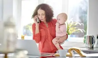 אישה במטבח שלה אוחזת תינוק תוך כדי שיחה בטלפון