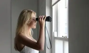 Mulher olhando pela janela com binóculos