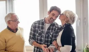 Mladý muž pri pohľade na telefón, jeho matka ho bozkávala a otec pri pohľade na ne