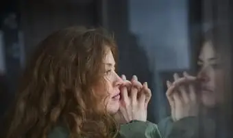 窓の外から自分の反射を見ている女性