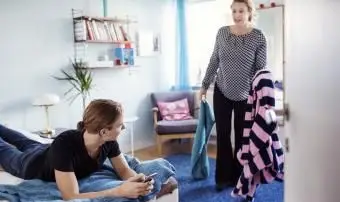 Donna arrabbiata che tiene i vestiti mentre guarda il figlio sdraiato sul letto