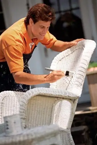 Uomo che dipinge sedia in vimini