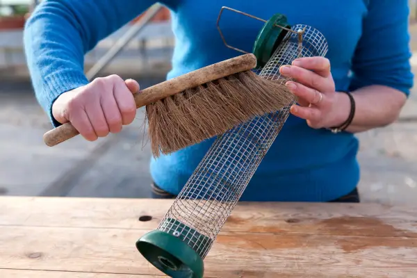 Cleaning a wire mesh bird feeder with a stiff brush