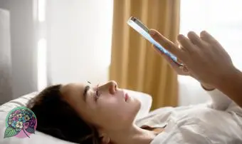 Mulher triste e cansada, deitada na cama enquanto envia mensagens de texto