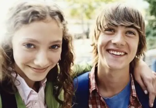 Teenager-Mädchen steht lächelnd mit ihrem Arm um ihren Freund