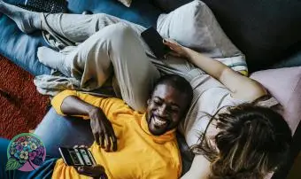 Veselý muž ležiaci na pohovke s priateľkou sediacou v obývačke doma