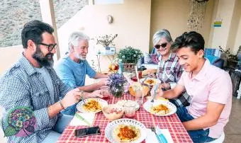 בני משפחה ארוחת צהריים יחד בחוץ על שולחן אדום - גילאים מעורבים דורות נהנים ונהנים עם פסטה איטלקית על המרפסת בבית - אבא סבא ובן