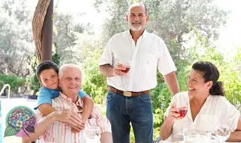 דיוקן של משפחה שמחה מתכנסת סביב שולחן אוכל בריא לארוחת צהריים אוכל בחוץ במהלך חופשת קיץ בבית גן נופש. כיף, אהבה וחיבה משפחה נהנית מהשמש, אורח חיים