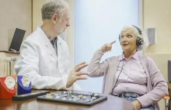 Paciente mayor usando audífonos y hablando con audiólogo