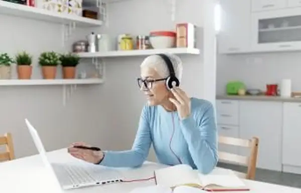 自宅でヘッドフォンとラップトップでオンライン学習する年配の女性