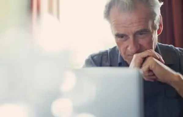 Älterer Mann mit gefalteten Händen mit Laptop