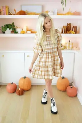 women wearing a plaid dress and boots in front of fall styled bookshelf