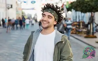 Jovem e bonito homem de barba vestido com roupas casuais elegantes, camiseta branca, jaqueta verde, bandana posando ao ar livre