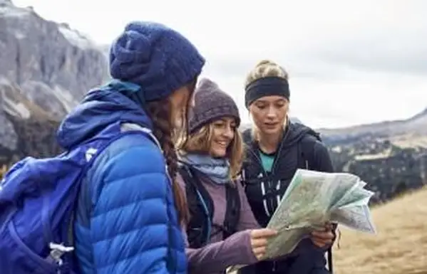 Tres mujeres jóvenes de senderismo en las montañas mirando el mapa