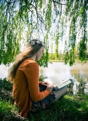수양 버드 나무 아래에 앉아 책을 가진 십 대