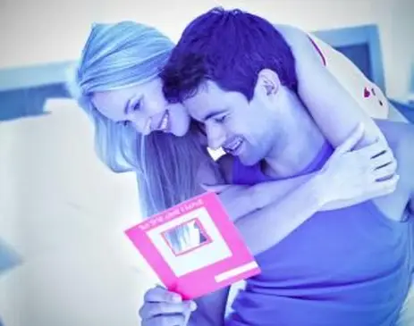 junges Paar liest eine Karte und umarmt sich auf einem Bett