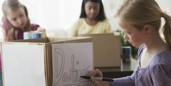 ילדה מציירת שלט תרומה על קופסת קרטון