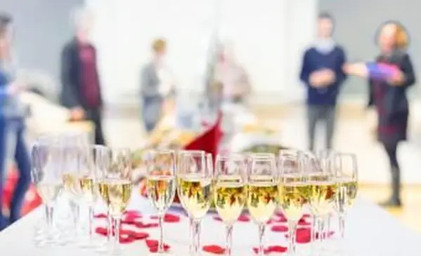 Banketové podujatie. Stôl s pohármi, občerstvením a kokteilmi. Ľudia oslavujúci v pozadí