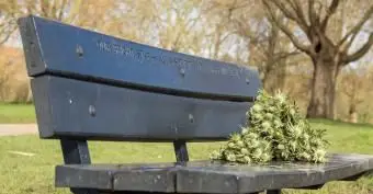 Banc commémoratif en bois avec de vieux bouquets de fleurs